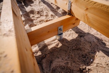 Açık hava inşaat projesinin bir parçası olan kumlu toprağa demirlenmiş ahşap tahta kaldırım destek iskeletinin yakın çekimi..