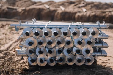 Kumlu bir şantiyedeki paletin üzerine yerleştirilmiş, yerleştirilmeye hazır büyük metal vidalardan oluşan yığının yakın görüntüsü..