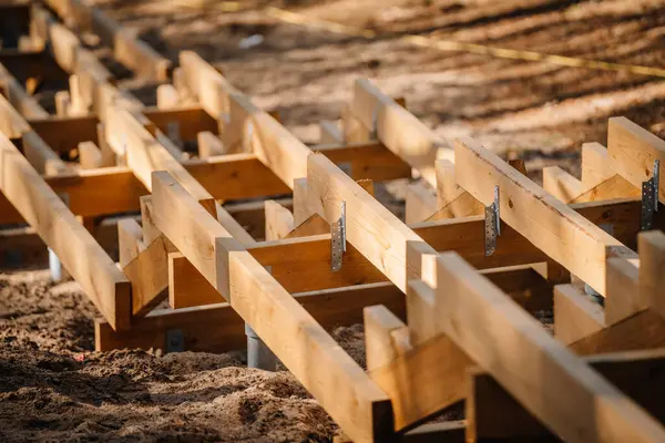 Kumlu zeminde yapım aşamasında olan ahşap merdiven iskeletine yakın plan, orman ortamında kirişler, parantezler ve metal destekler görülüyor..