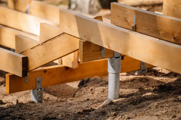 Orman bölgesinde inşaat halindeki ahşap merdivenlere yakın çekim. Metal zemine monte edilmiş destek kirişleri kumlu toprakta emniyette..