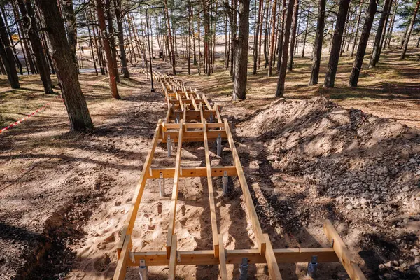 Tahta merdiven iskeleti kumlu bir orman tepesinde, ağaçlar ve dikkat bantlarıyla çevrili, uzaktaki sahile doğru gidiyor..