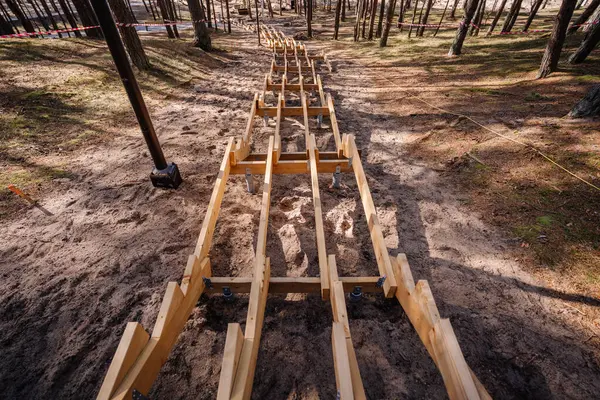 Metal direklerle desteklenen ormanlık kumlu bir yamaçta ahşap merdiven, dikkat bandı ve bölgeyi çevreleyen ağaçlarla birlikte..