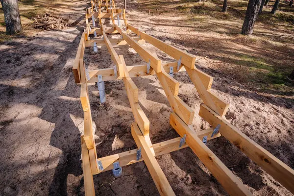 Görünür metal vida desteğiyle ve ahşap çerçeve yapısıyla kumlu bir orman yamacında inşaat halindeki ahşap merdiven..