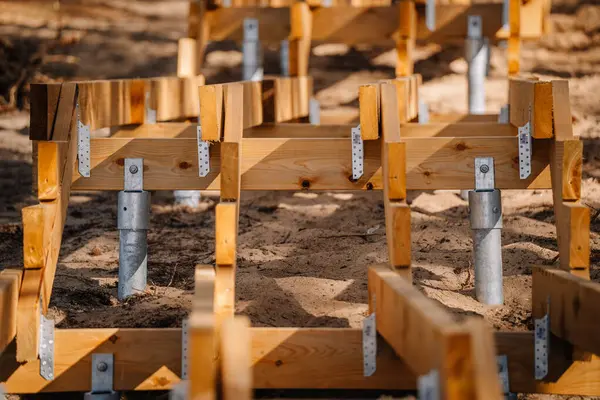 Orman bölgesinde yapım aşamasındaki ahşap bir merdivenin yakın çekimi, galvanize vida yığınları ve kumlu arazide metal parantezler tarafından destekleniyor..