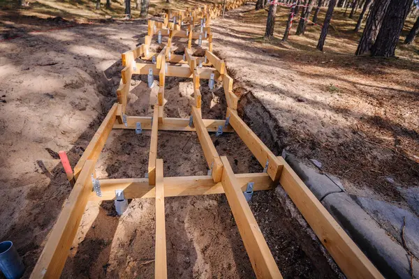 Kum ve çam ağaçlarıyla çevrili görünür vida yığını temelleri ve metal parantezleri ile bir ormanda yapım aşamasındaki ahşap iskelet..