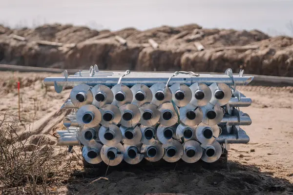 Kumlu bir şantiyedeki paletin üzerine yerleştirilmiş, yerleştirilmeye hazır büyük metal vidalardan oluşan yığının yakın görüntüsü..