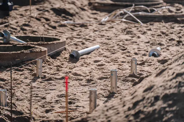 Metal zemin vidaları yakın çekim bir inşaat sahasında kumlu toprak kısmen yüklü temel pozisyonlarını işaretleyen sicim hatları.