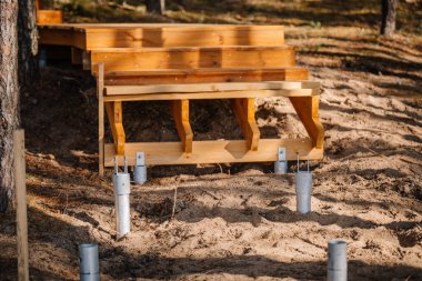 Kumlu arazide yapım aşamasındaki ahşap merdivenler görünür metal zemin çapaları ile ormandaki destek direklerine hazırlanıyor..