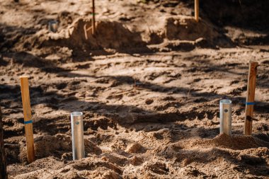 Metal zemin kolları kısmen kumlu toprağa monte edilmiş, açık hava inşaat sahasının temel düzeni için ahşap kazıklarla işaretlenmiş..