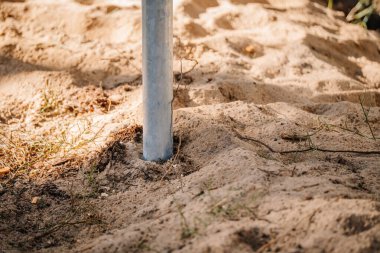 Orman çevresindeki bir inşaat temelinin parçası olan kumlu toprağa gömülü galvanize çelik vida yığınının yakın çekimi.