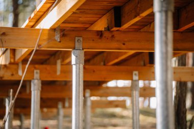 Orman ortamındaki galvanize çelik vida yığınları tarafından desteklenen yüksek ahşap kaldırım yapısının yakın görüntüsü..