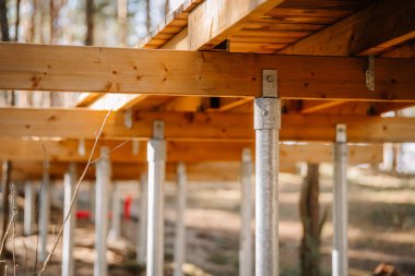 Orman ortamındaki galvanize çelik vida yığınları tarafından desteklenen yüksek ahşap kaldırım yapısının yakın görüntüsü..