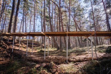 Ormanda inşaat halindeki ahşap kaldırım. Uzun çam ağaçlarıyla çevrili düz kumlu zemindeki metal vida yığınlarıyla destekleniyor..