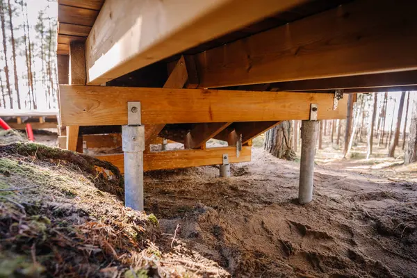İnşaat sırasında kumlu bir ormanlık alanda bulunan galvanize çelik vida yığınları üzerine inşa edilmiş ahşap güverte temelinin yakın görüntüsü..