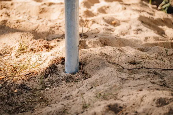 Orman çevresindeki bir inşaat temelinin parçası olan kumlu toprağa gömülü galvanize çelik vida yığınının yakın çekimi.