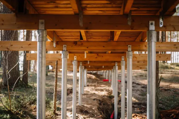 Ormandaki bir alanda galvanize çelik tornavida desteğiyle desteklenen ahşap kaldırımın altında yakın plan görüntü, yapısal destek ve temel detaylarını gösterir..