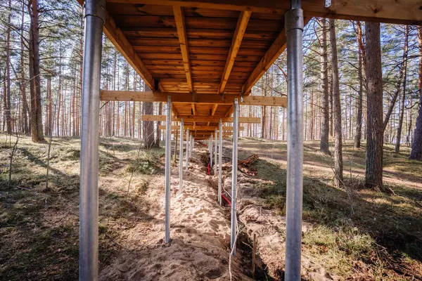 Ormanda yapım aşamasındaki tahta kaldırım manzarasının altında galvanize çelik vida yığınları ve kumlu toprak ve ağaçlarla çevrili..