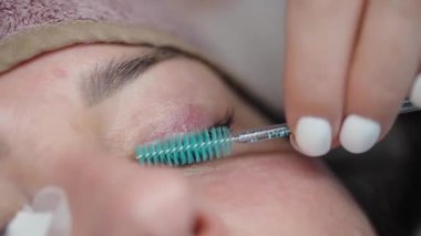Bir güzellik uzmanının uygulamadan sonra kirpik eklentilerini mavi bir hortlakla fırçalaması, kirpik hizalaması ve güzellik salonu ortamında parlak bir görünüm sağlaması..
