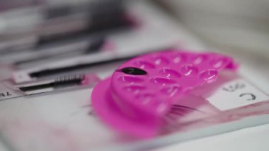 Profesyonel kirpik uygulama prosedürlerinde kullanılan pembe bir yapıştırıcı paletine siyah kirpik yapıştırıcı batıran bir cımbız videosu..