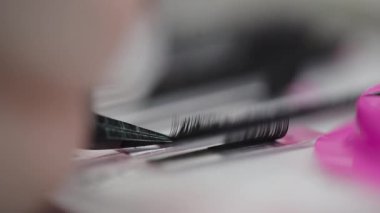 Bir tepsiden bireysel kirpik uzantılarını kavrayan cımbızların aşırı yakın çekimi, güzellik tedavi ortamında kırbaç uygulamasına hazırlanıyor.