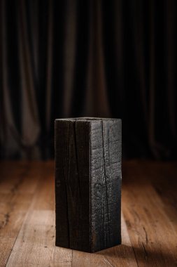 Kömürleşmiş ahşap bir vazo ya da pürüzlü bir dokusu olan içi boş bir blok, arka planda koyu perdeleri olan ahşap bir zeminde duruyor. Ahşap temasını yak.