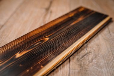 Açık ahşap bir zemine yerleştirilmiş tahıl ve düğümlerle tek bir yanmış tahtanın yakın çekimi. Ayrıntılı doku doğal kömürleşmeyi vurguluyor.