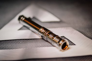 Valmiera, Letonya - 16 Şubat 2022 - Arkaplanda beyaz geometrik elementler bulunan desenli bir yüzeye yerleştirilmiş düğme detaylarıyla metalik enerji kılıcı kabzasının yakın çekimi.