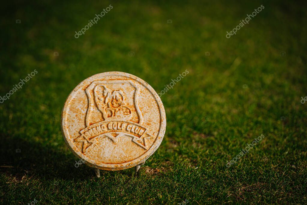 Belek, Turkey - February, 25, 2025 - A round, weathered stone tee marker set on green grass at a golf course, showing a sculpted emblem design with vintage character.