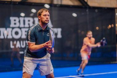 Riga, Letonya - 5 Nisan 2025 - Odaklanmış erkek padel oyuncusu kapalı mavi bir sahada bir maç için hazırlık yapıyor..
