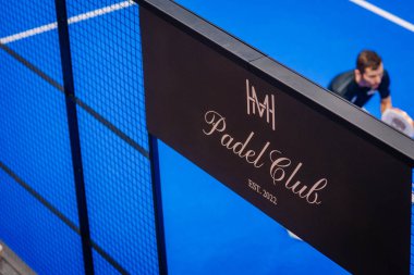 Riga, Letonya - 5 Nisan 2025 - Logosu ve EST yazılı siyah Padel Club afişinin yakın görüntüsü. 2022 metin, bir padel oynatıcı eylem arka planda hafifçe bulanık