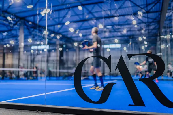 Riga, Letonya - 5 Nisan 2025 - Padel turnuvası sırasında, camda büyük bir GaR logosu bulunan oyuncularla birlikte bir padel kortunun camından bakın