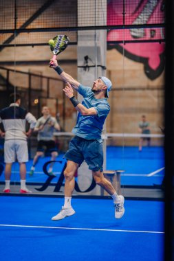 Riga, Letonya - 5 Nisan 2025 - Erkek padel oyuncusu bir padel turnuvasında atlamak için yükseğe sıçradı, çeviklik ve güçlü atletik performans sergiledi..