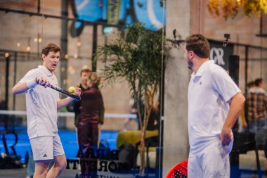 Riga, Letonya - 5 Nisan 2025 - Beyaz elbiseli iki erkek Padel turnuvası sırasında iç saha sahasında rahat durarak strateji ya da oyun hakkında tartıştılar.