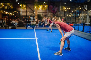 Riga, Letonya - 5 Nisan 2025 - Kırmızı tişörtlü iki bayan padel oyuncusu bir sonraki servis için hazırlanıyor..