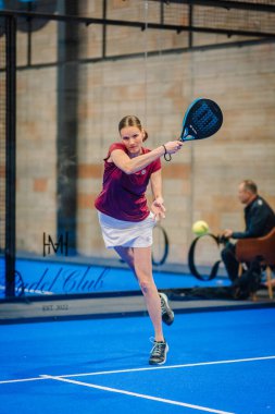Riga, Letonya - 5 Nisan 2025 - Odaklanmış kadın padel oyuncusu, bir padel turnuvası sırasında bir forehand vuruşuyla karşılık veriyor,.