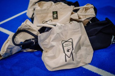 Riga, Letonya - 5 Nisan 2025 - Rudys Kombucha damgalı çantalar padel turnuvası sırasında mavi bir padel kortu zeminine yerleştirildi