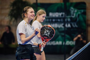 Riga, Letonya - 5 Nisan 2025 - Padel turnuvası sırasında ağda heyecan ve neşe gösteren iki genç bayan padel oyuncusu.
