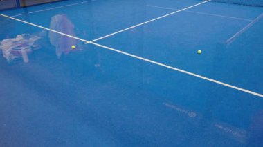 Riga, Letonya - 5 Nisan 2025 - Padel turnuvası sırasında yakalanan iki sarı top, arka planda görünür teçhizat ve havlularla mavi bir padel kortunda dinleniyor. Yavaş çekim videosu.
