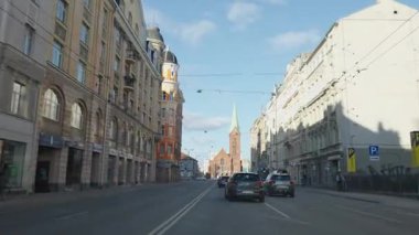 Riga, Letonya - 5 Nisan 2025 - Tarihi mimarisi ve önde gelen kırmızı tuğlalı kilisesi olan bir Avrupa şehrinden geçiyor..