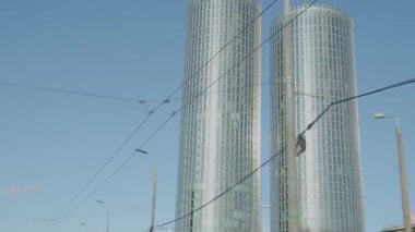 Riga, Letonya - 5 Nisan 2025 - Temiz mavi gökyüzü altında cam cepheli modern ikiz gökdelenler, hareket halindeki şehir mimarisi sırasında hareket halindeki bir arabadan izlendi.