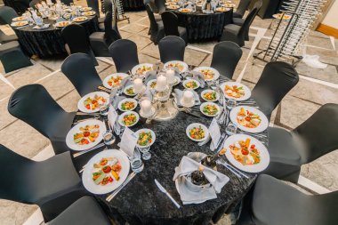 Türkiye, Belek - 28 Şubat 2025 - Ödül töreni yemeği için verilen zarif yuvarlak ziyafet masası, gurme başlangıçlar, mum süslemeler ve siyah sandalye örtüleri.