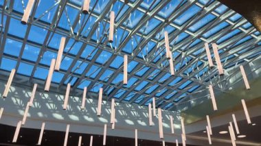 Riga, Letonya - 5 Nisan 2025 - Dekoratif ışıkları ve yukarıda açık mavi gökyüzü olan modern alışveriş merkezinin cam tavanına yakından bakın.