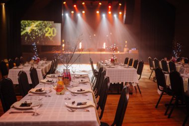 Valmiera, Letonya - 13 Aralık 2024 - Süslü yemek masaları, şenlikli ışıklandırma, sahne ışıkları ve samimi kutlama atmosferi ile VU 'nun 20. yıldönümü için şık bir şölen salonu..