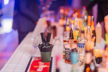 Valmiera, Letonya - 13 Aralık 2024 - Çeşitli alkol şişeleri, kokteyl malzemeleri ve renkli ışıklı şenlikli parti atmosferinde pipet içme tezgahı.