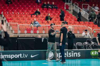 Riga, Letonya - 12 Nisan 2025 - Bir maçtan sonra iki erkek sahada el sıkışırken, bir kadın kapalı bir spor salonundaki finaller sırasında el çırpıyor.