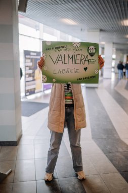 Riga, Letonya - 12 Nisan 2025 - Fan kapalı bir arena koridorunda oynanan florbol finallerinde Valmiera takımını destekleyen bir tabela tutuyor.