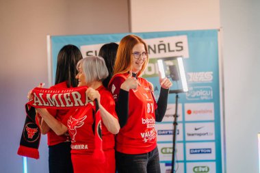 Riga, Letonya - 12 Nisan 2025 - Kırmızı formalı bir grup bayan zemin topu fanatiği, 360 video kabini deneyiminin keyfini çıkarıyor..