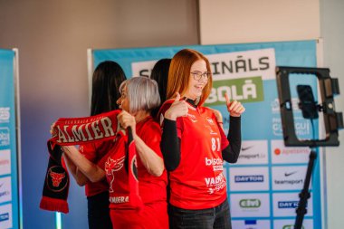 Riga, Letonya - 12 Nisan 2025 - Kırmızı formalı bir grup bayan zemin topu fanatiği, 360 video kabini deneyiminin keyfini çıkarıyor..