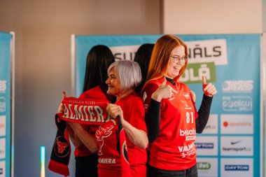 Riga, Letonya - 12 Nisan 2025 - Kırmızı formalı bir grup bayan zemin topu fanatiği, 360 video kabini deneyiminin keyfini çıkarıyor..