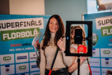 Riga, Letonya - 12 Nisan 2025 - Xiaomi Arena 'daki finaller sırasında 360 video kabininde üç gülümseyen bayan florbol taraftarı poz verdi.